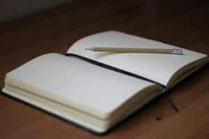 An open book, laying flat on a table. The pages are blank, and a pencil lies on the page, waiting to write.