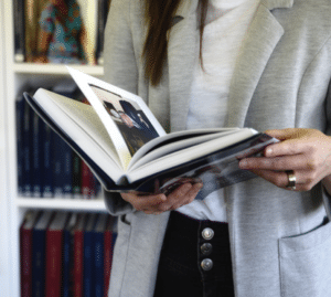 A standing woman, holding open a book.