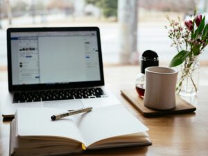 A photograph of a laptop, a notebook, a pen and a mug of tea on a table.