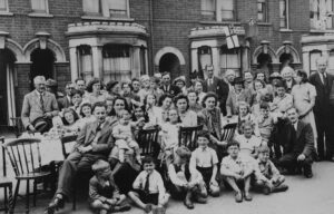 A photograph of a group of people having a street party in front of terraced houses in 1940s England.