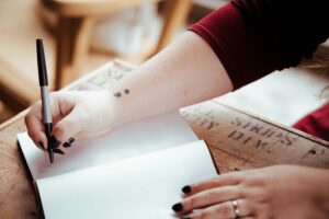 A close up image of someone's forearm and hand as they write into an empty notebook.